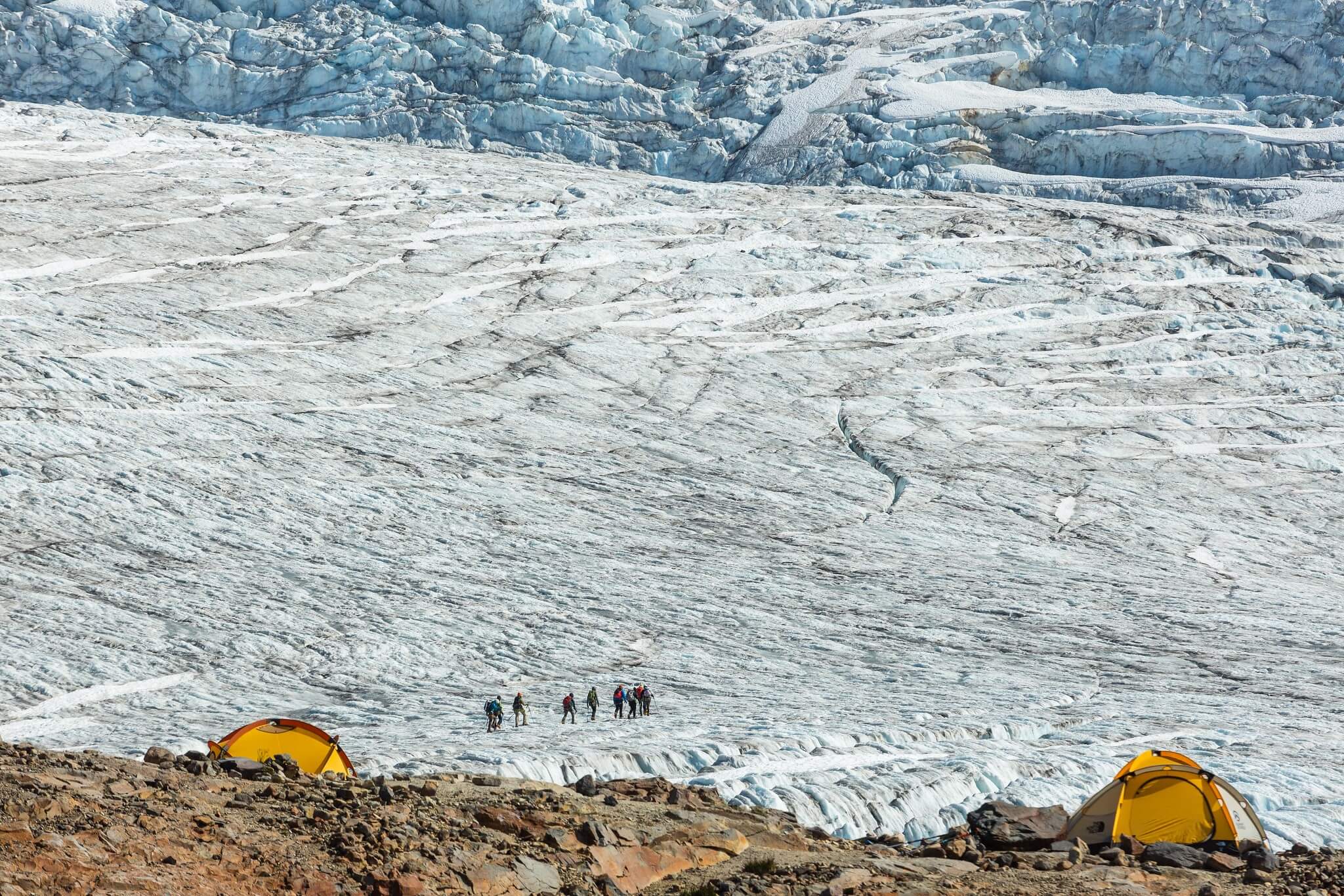 mountain climbers walk up snowy mountain away from camp